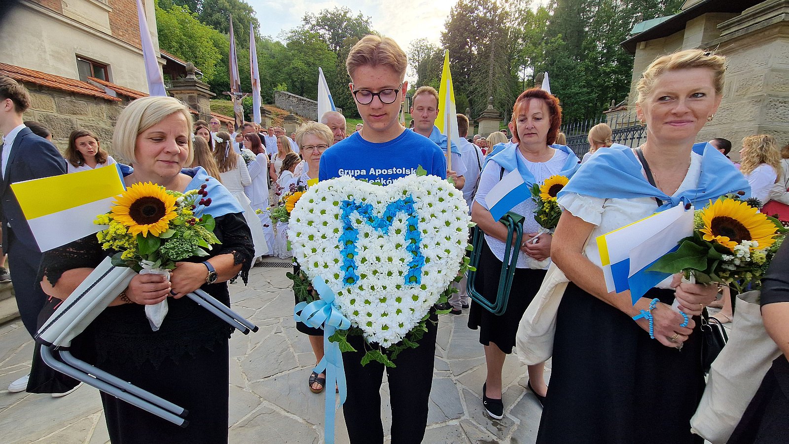 Serce z białych kwiatów z literą M i słoneczniki.